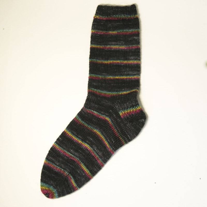 dark hand knit sock with the dark colour broken by a short run of gold, turquoise and pink 