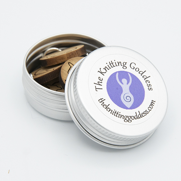 small round tin with The Knitting Goddess logo. Tin is open showing stich markers inside it.