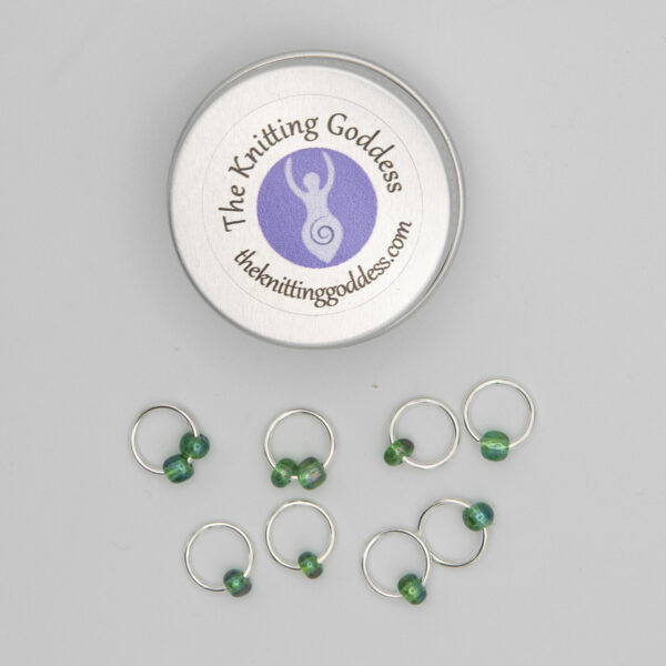 set of eight stitch markers made with jump rings and green beads. Shown with a small round storage tin with The Knitting Goddess logo