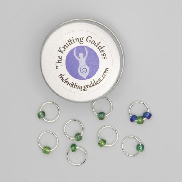 set of eight stitch markers made with jump rings and green and blue beads. Shown with a small round storage tin with The Knitting Goddess logo