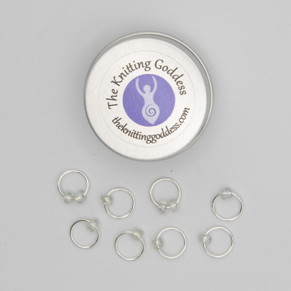 set of eight stitch markers made with jump rings and pearl beads. Shown with a small round storage tin with The Knitting Goddess logo