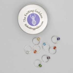 set of eight stitch markers made with jump rings and beads. Shown with a small round storage tin with The Knitting Goddess logo