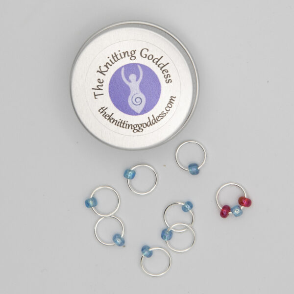set of eight stitch markers made with jump rings and turquoise and red beads. Showne with a small round storage tin with The Knitting Goddess logo