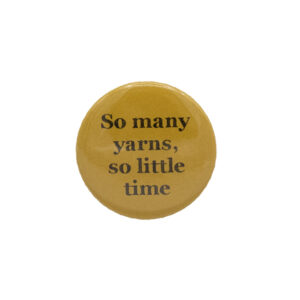 Yellow button badge with black writing which reads So many yarns, so little time