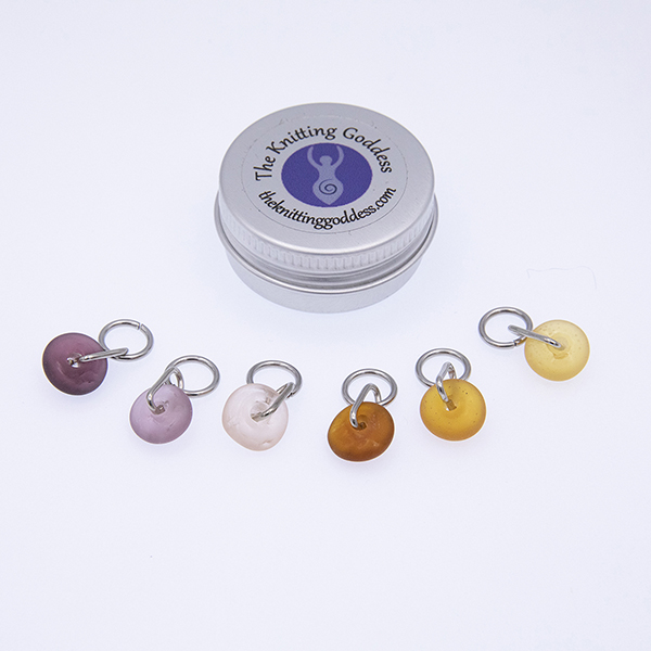 six plum and copper glass stitch markers with a round storage tin