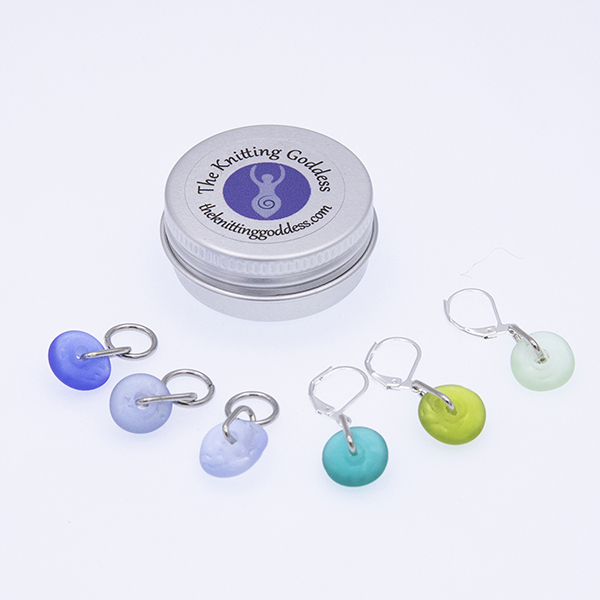 six blue and green glass stitch markers with a round storage tin