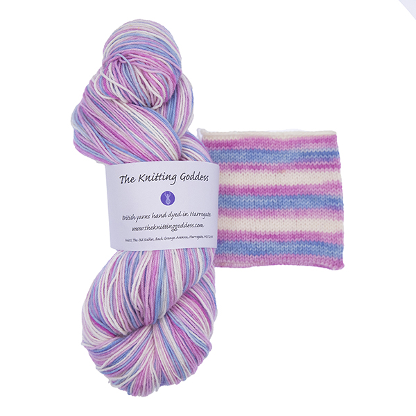 skein of hand dyed multicolour yarn with trans flag colours - pink, white and blue. Shown with swatch showing how the stripes knit up. Skein has a ball band from The Knitting Goddess