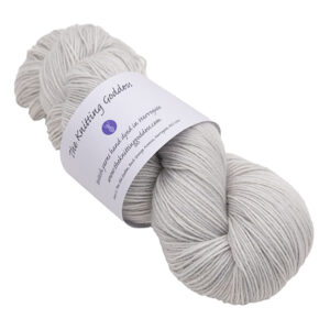 a skein of very pale gray pearl hand dyed BFL nylon sock yarn with The Knitting Goddess ball band