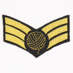 embroidered patch on black felt, embroidery in golden yellow. Design is three chevron stripes with a ball of yarn on top..