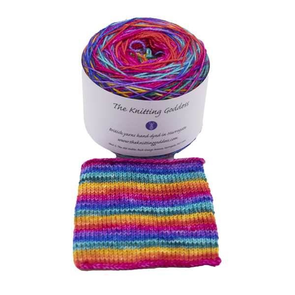 A yarn cake with The Knitting Goddess ball band. Yarn is hand dyed in rainbow colour Swatch shows how the yarn knits up in stripes f one or two rounds of a sock.