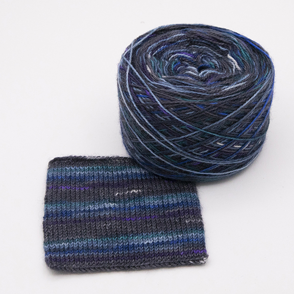 ball and knitted sample of self striping sock yarn with dashes of green, blue, purple and white on black and navy