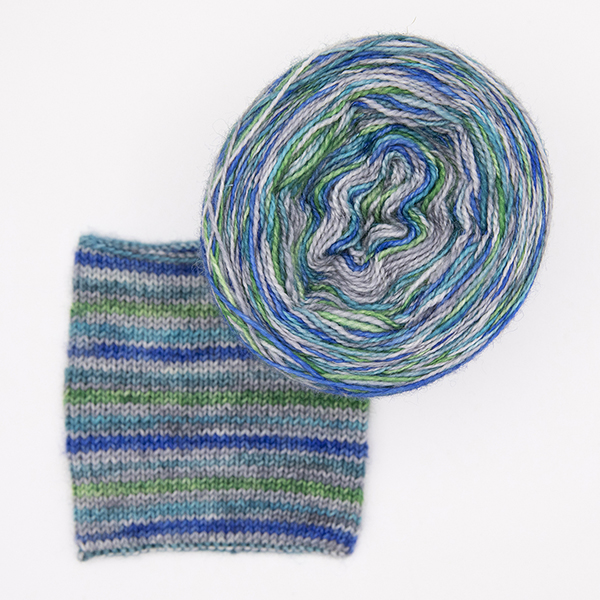 ball and knitted sample of self striping sock yarn with greens, blues and silver, top view