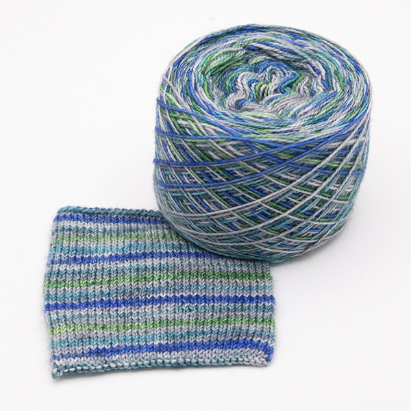 ball and knitted sample of self striping sock yarn with greens, blues and silver