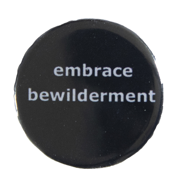 black pin badge with text "embrace bewilderment"