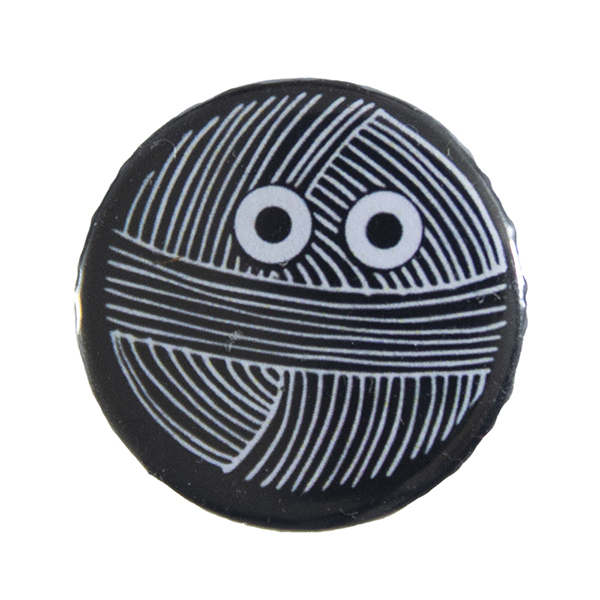 black pin badge with line drawing of a ball of yarn with eyes