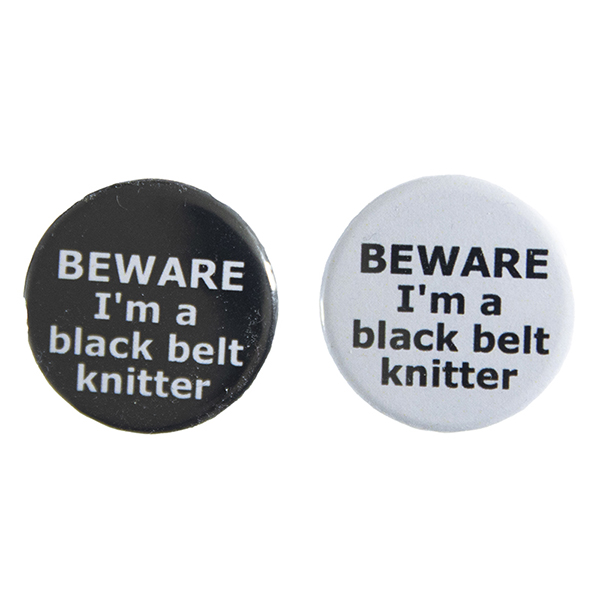 pin badges with text "BEWARE I'm a black belt knitter". Badges are black and light grey