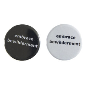 pin badges with text "embrace bewilderment". Badges are black and light grey