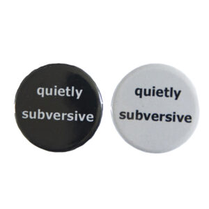 pin badges with text "quietly subversive". Badges are black and light grey