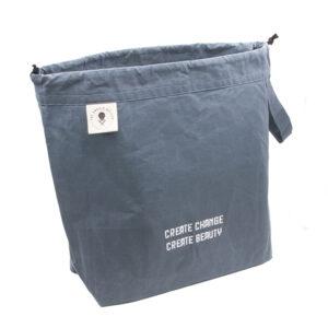 large drawstring project bag in slate blue fabric, wrist strap, drawstring closure, screen printed with text "CREATE CHANGE CREATE BEAUTY"
