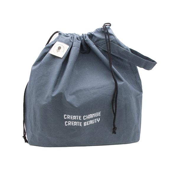 large drawstring project bag in slate blue fabric, wrist strap, drawstring closure, screen printed with text "CREATE CHANGE CREATE BEAUTY", drawstring pulled closed