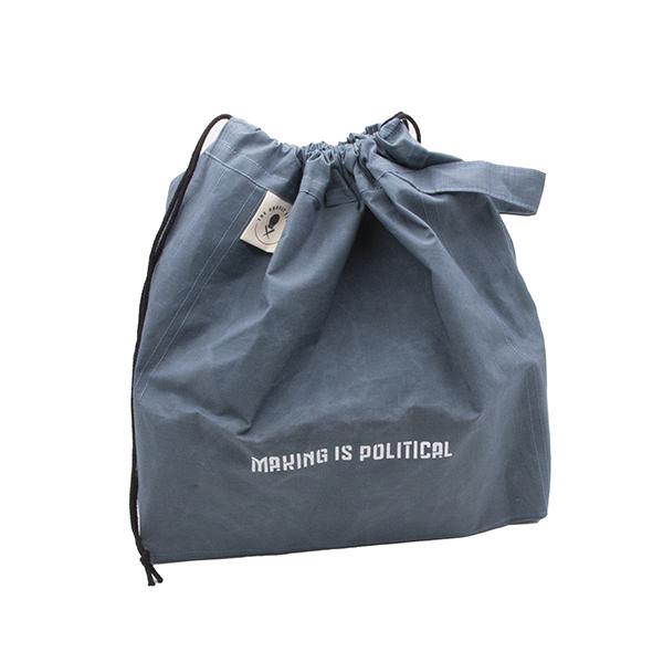 large drawstring project bag in slate blue fabric, wrist strap, drawstring closure, screen printed with text "MAKING IS POLITICAL" shown with drawstrings closed