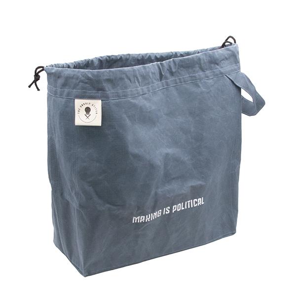 large drawstring project bag in slate blue fabric, wrist strap, drawstring closure, screen printed with text "MAKING IS POLITICAL"