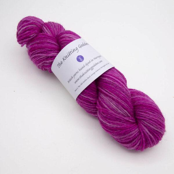 raspberry hand dyed sock yarn, wound up in a skein with The Knitting Goddess ball band