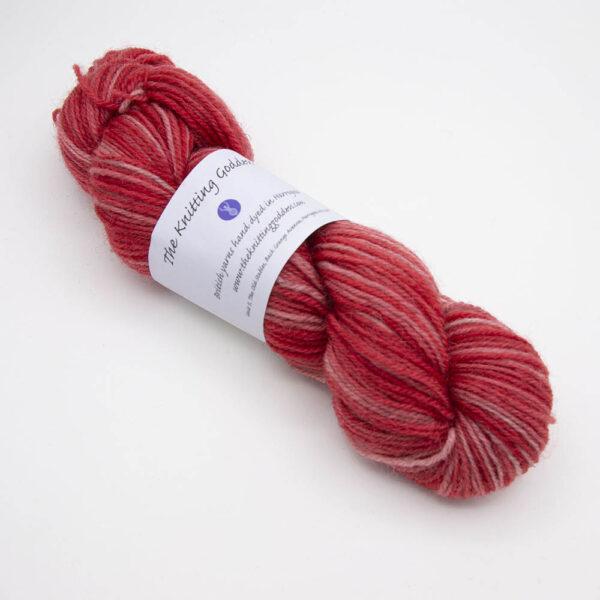 red hand dyed sock yarn, wound up in a skein with The Knitting Goddess ball band