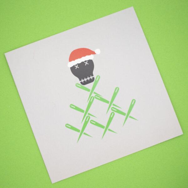 The Unruly Stitch christmas gift card, a black skull wearing santa hat on top of tree made from green sewing needles