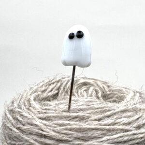white glass ghost pin, point stuck into a ball of yarn so the shaft is visible