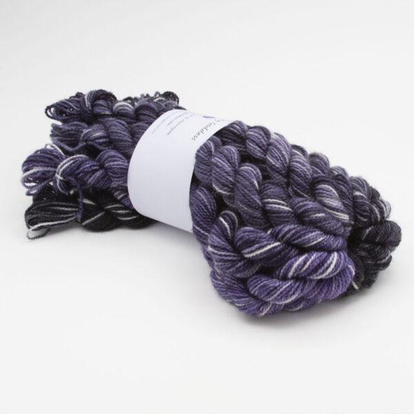 set of 12 mini skeins in all the stars in the sky colourway. Skeins go from purple to black and all have white splodges.Skeins are tied in a bundle with The Knitting Goddess ball band.