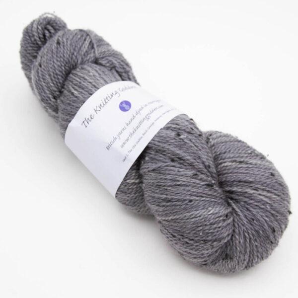 skein of charcoal grey coal tweed yarn with dark flecks and The Knitting Goddess ball band
