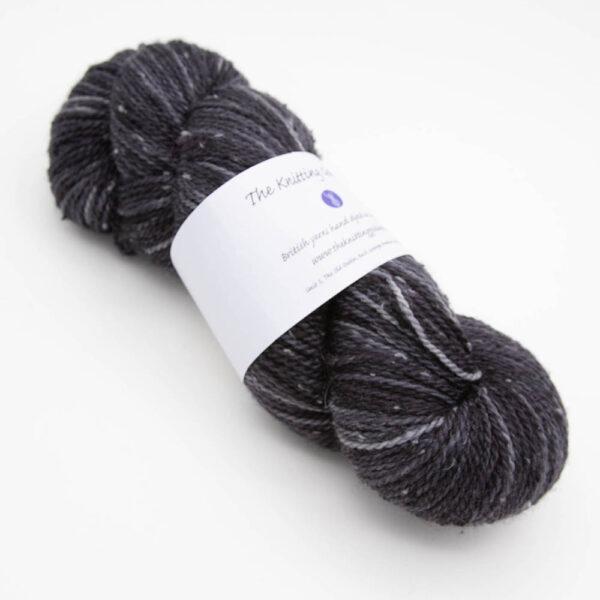 skein of very dark grey coal tweed yarn with dark flecks and The Knitting Goddess ball band