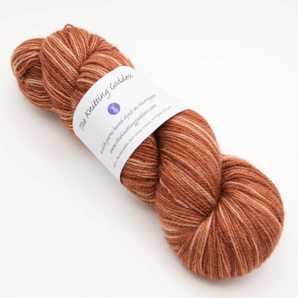 skein of copper Bluefaced Leicester and nylon yarn which has a high twist and The Knitting Goddess ball band