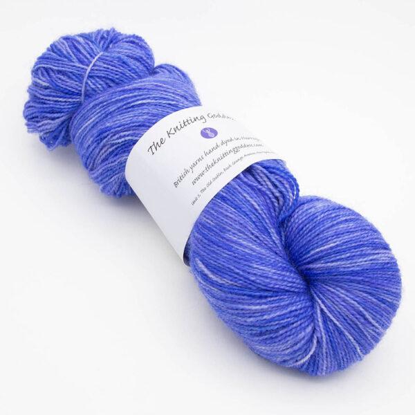 skein of cornflower blue ( blue with a little purple) Bluefaced Leicester and nylon yarn which has a high twist and The Knitting Goddess ball band