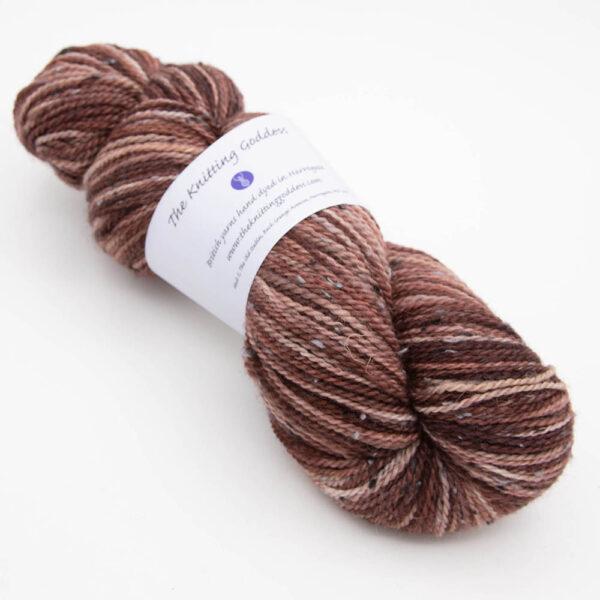 skein of dark copper tweed yarn with dark flecks and The Knitting Goddess ball band