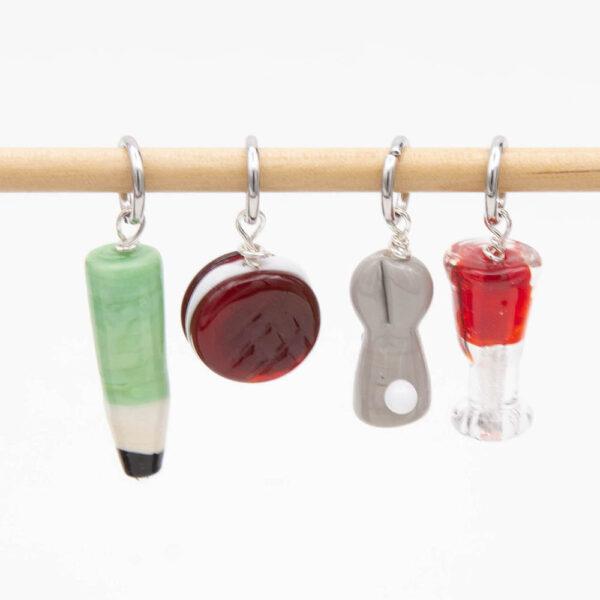 back view of lampwork glass stitch markers with jump rings. Glass of red wine, bunny, biscuit and pencil.