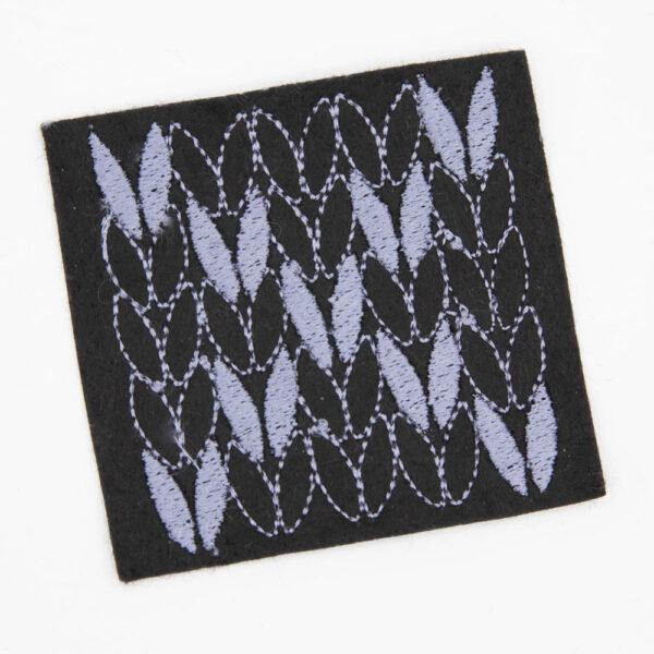 embroidered patch on black felt. Patch has 5 rows of 5 stocking stitches, and the stitches of both diagonals have been filled to create a cross
