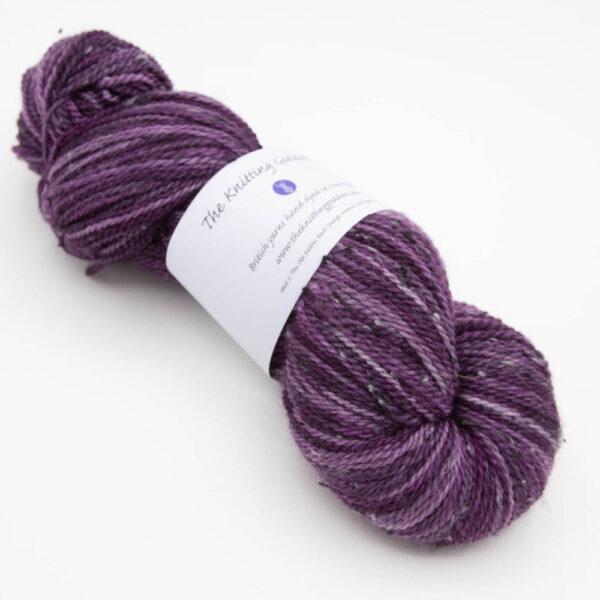 skein of plum tweed yarn with dark flecks and The Knitting Goddess ball band
