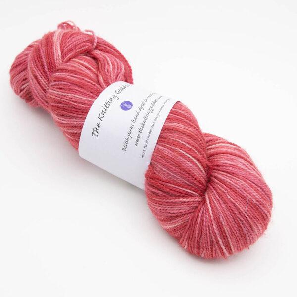 skein of red Bluefaced Leicester and nylon yarn which has a high twist and The Knitting Goddess ball band