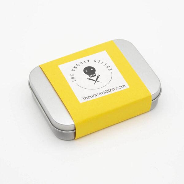 metal tin with yellow band ans The Unruly Stitch logo