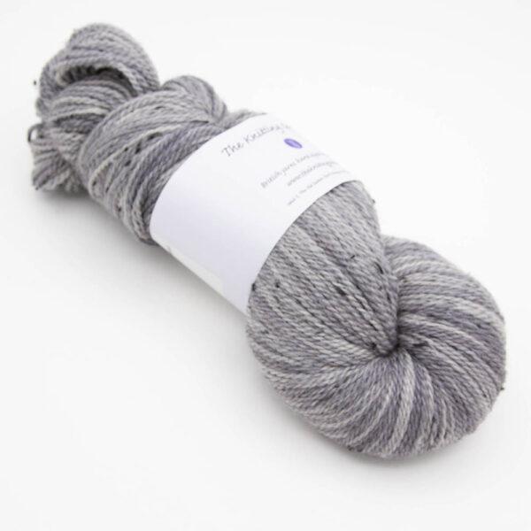 skein of silver tweed yarn with dark flecks and The Knitting Goddess ball band