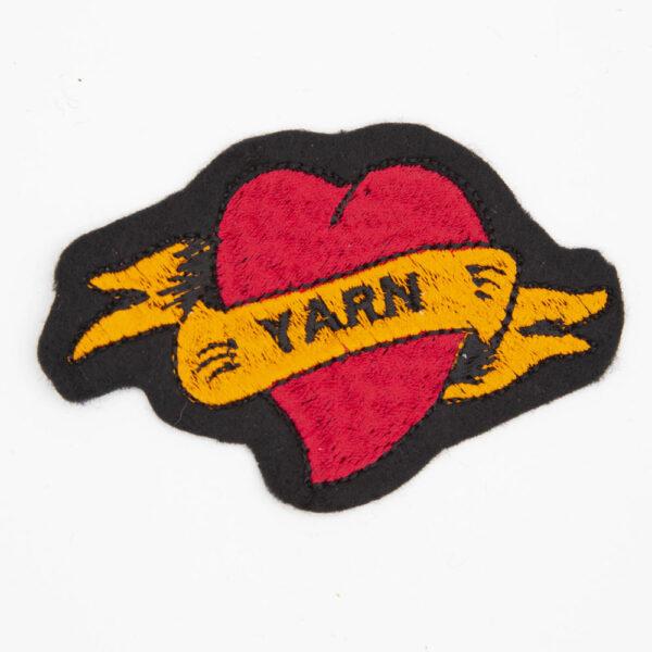 red tattoo style heart patch with orange banner, embroidered onto black felt. Banner ha the text YARN
