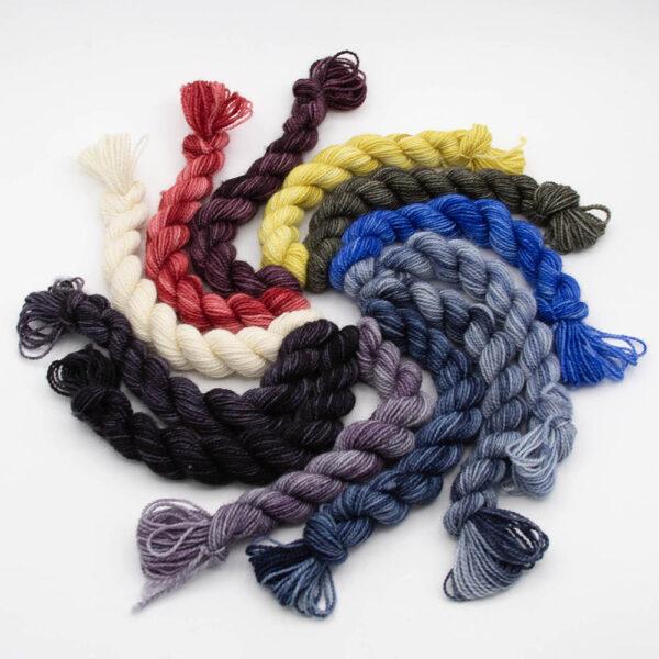 12 mini skeins in a spiral. Colours are 3 greys, 3 slates, blue, 2 yellows, 2 reds and white