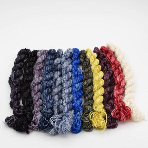 12 mini skeins in a row. Colours are 3 greys, 3 slates, blue, 2 yellows, 2 reds and white