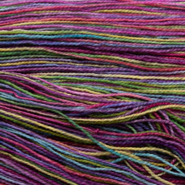 close up of hand dyed black rainbow yarn with gold, green, turquoise, purple, pink and orange overdyed with black.