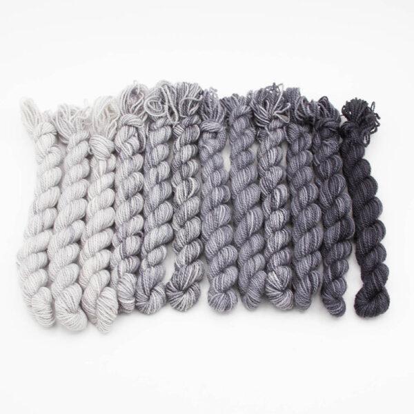 set of 12 mini skeins dyed in a grey fade arranged in a row