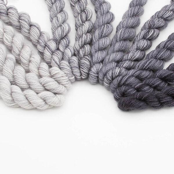 set of 12 mini skeins dyed in a grey fade arranged in a curve