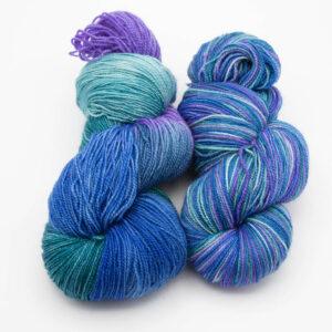 hand dyed kingfisher yarn in blue, purple and green. Two skeins side by side, one as dyed, the other reskeined.