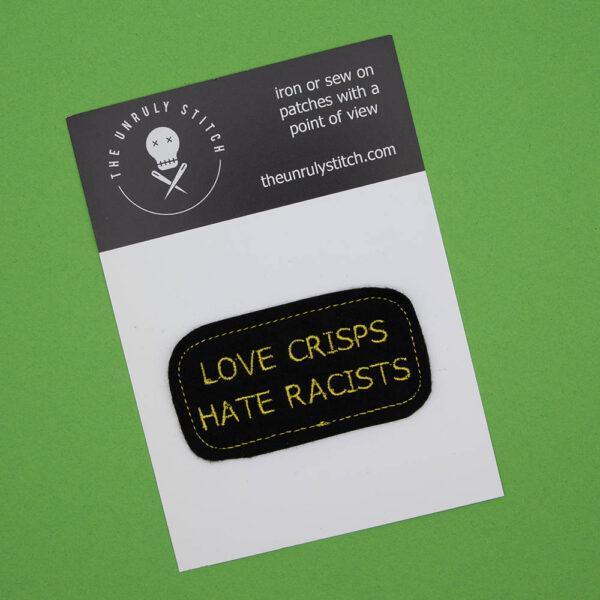 embroidered iron on patch on a postcard. Patch is embroidered onto black felt with yellow thread and reads LOVE CRISPS HATE RACISTS